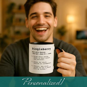 Pode incluir: Uma caneca de cerâmica branca com uma borda e uma alça pretas. A caneca tem uma definição da palavra "Dingleberry" impressa nela. A definição está em uma fonte de máquina de escrever. A caneca está sendo segurada pela mão de uma pessoa.