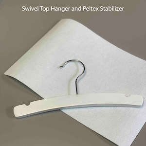 May include: White wooden hanger with a swivel top hook. The hanger is on top of a white felt sheet. The text "Diaper Stacker Sewing Pattern" and "Swivel Top Hanger and Peltex Stabilizer" is visible above the hanger.