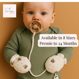 May include: An olive green long-sleeve bodysuit with white mittens featuring a yellow and black bee pattern. A beige pacifier is attached to a braided white cord. Text on the image reads: The Cajun girl, Available in 8 Sizes Premie to 24 Months.