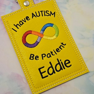 Peut inclure: Porte-clés en cuir jaune avec le texte "I have Autism" et un symbole d'infini aux couleurs de l'arc-en-ciel. Le texte "Be Patient" et le nom "Eddie" sont également sur le porte-clés.