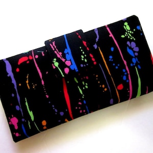May include: Black wallet with a colorful paint splatter design. The wallet has a flap closure and is made of fabric.