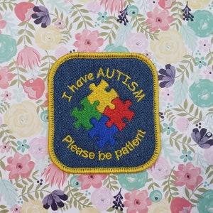 May include: Blue denim patch with yellow stitching, featuring a puzzle piece design and the text "I have Autism Please be patient".