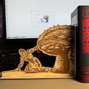 May include: A wooden bookend featuring a detailed engraving of a figure struggling against a large creature. The bookend is positioned next to three black books with the word "BERSERK" in red lettering.
