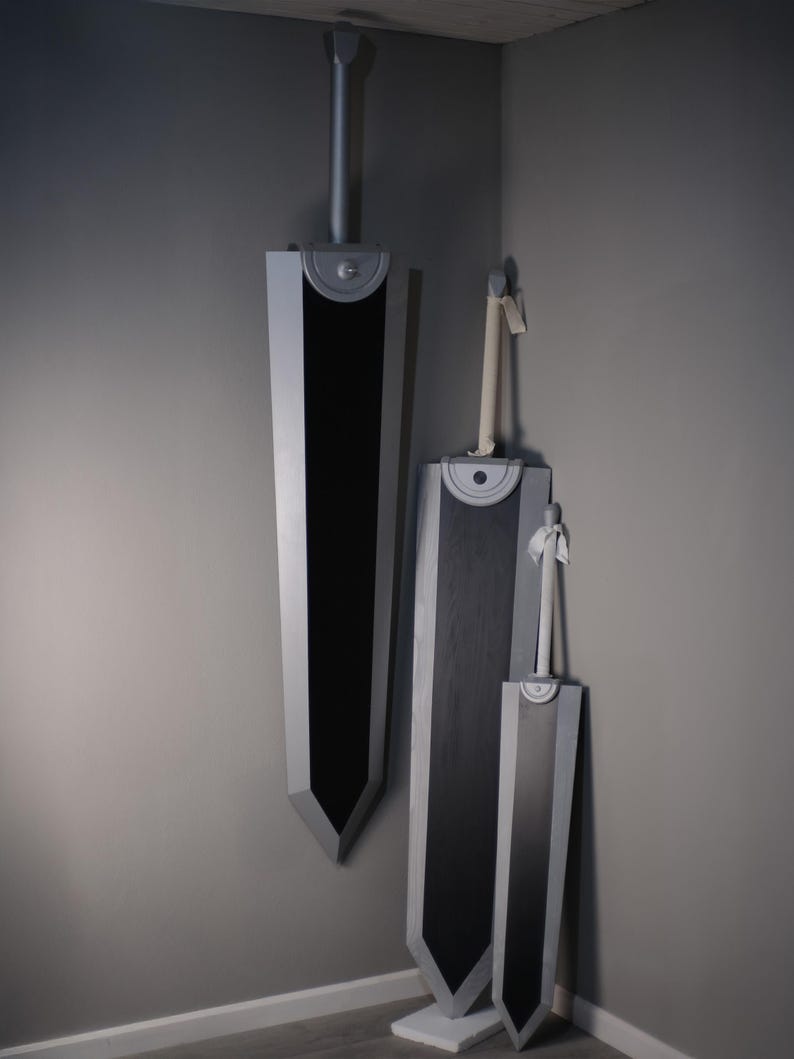 May include: Three large, heavy-duty swords of varying sizes displayed in a corner. Each sword features a wide, flat black blade with silver-colored edges, a circular silver guard, and a long cylindrical handle. The handles have light-colored fabric wraps.