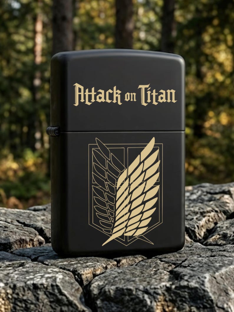 May include: Black lighter with the text "Attack on Titan" in gold lettering. The lighter features a gold emblem of wings on the front. The lighter is sitting on a tree stump.
