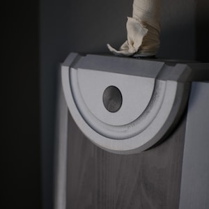May include: A large sword with a dark grey blade and a silver semi-circular guard featuring a central black circular detail. The handle is wrapped in a light beige fabric bandage, extending upwards from the top of the silver guard section.