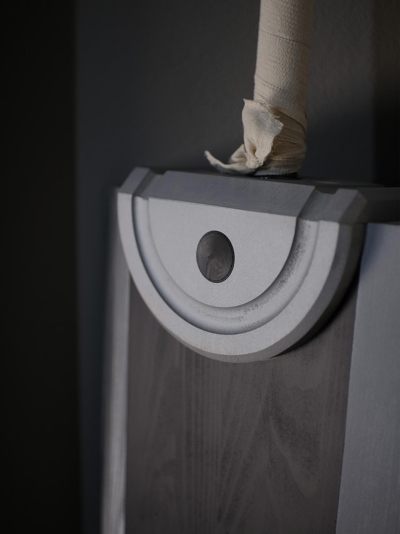 May include: A large sword with a dark grey blade and a silver semi-circular guard featuring a central black circular detail. The handle is wrapped in a light beige fabric bandage, extending upwards from the top of the silver guard section.