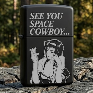 Puede incluir: Encendedor negro con el texto "SEE YOU SPACE COWBOY..." en blanco. El encendedor presenta una ilustración en blanco y negro de una mujer. El encendedor está sobre una roca.