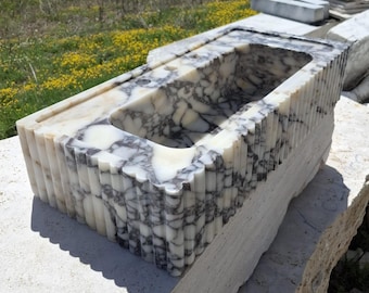 May include: A rectangular marble sink featuring a white and dark gray veined pattern with a polished finish. The exterior sides of the basin are carved with vertical fluted detailing, and the top surface includes two pre-drilled faucet holes.