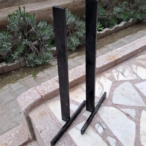 May include: Two black metal shelf brackets with a simple L-shaped design. The brackets are made of sturdy metal and have a black powder-coated finish.