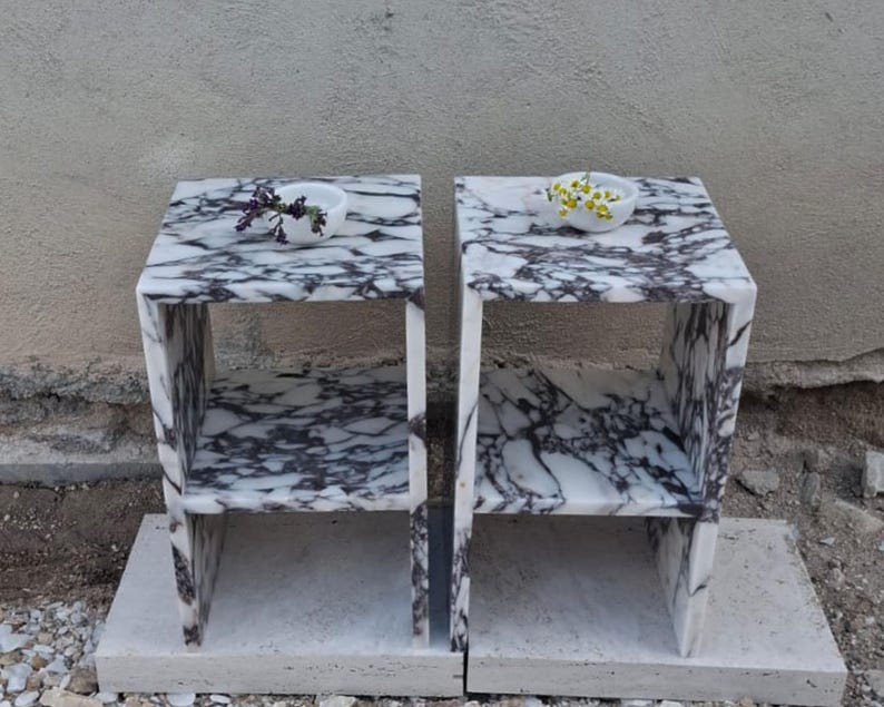 Puede incluir: Dos mesas auxiliares de m&aacute;rmol blanco con un estante. Cada mesa tiene un peque&ntilde;o cuenco blanco en la parte superior con flores secas.