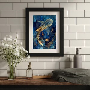 May include: Framed art print featuring a watercolor painting of a whale shark swimming in a deep blue ocean. The artwork has gold and orange accents, and is set in a black frame. The print is displayed on a wooden shelf with bathroom accessories.