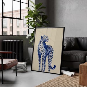 May include: A framed wall art print featuring a stylized blue cheetah with a spotted pattern on a solid beige background. The cheetah is depicted in a standing position, facing toward the right side of the frame with its head turned slightly.