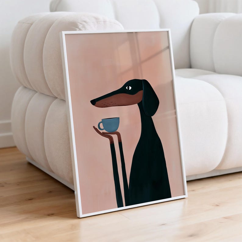 May include: A framed wall art print featuring a stylized illustration of a black and brown dog with long limbs holding a small blue coffee cup. The dog is set against a solid, muted peach-colored background, enclosed in a thin white frame.