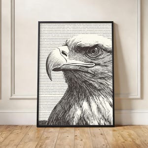May include: Black and white framed print of an eagle's head in profile. The eagle is rendered in a detailed, vintage style with a textured background of horizontal lines. The artwork is displayed on a wooden floor.