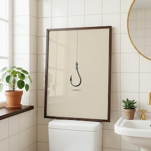 May include: A framed wall art print featuring a minimalist illustration of a single black fishing hook suspended by a thin line against a solid light beige background. The artwork is enclosed in a simple dark brown wooden frame.