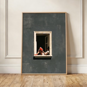May include: A framed vertical wall art print featuring a dark grey textured wall with a centred rectangular window. A person sits inside the window frame reading an open book with a bright orange cover, wearing light clothing and orange shoes.