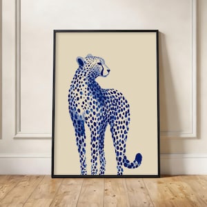 May include: A framed art print featuring a blue cheetah illustration on a cream background. The cheetah is depicted with dark blue spots and a black frame. The artwork is displayed on a wooden floor.