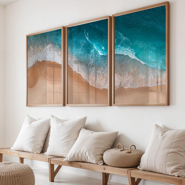 May include: A triptych wall art set featuring an aerial view of a sandy beach with turquoise ocean waves crashing against the shore. Each of the three rectangular prints is encased in a light-toned wooden frame, displaying a continuous coastal scene.