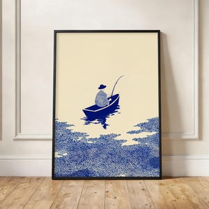 May include: A framed vertical art print featuring a blue and cream illustration of a person in a small boat fishing on water. The lower portion of the print is filled with a dense, stippled blue pattern representing water, while the upper portion is a solid cream color.