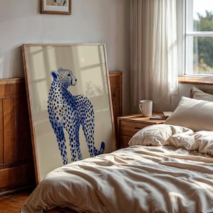 May include: A large rectangular framed wall art print featuring a stylized illustration of a cheetah. The cheetah is rendered in shades of deep blue with a distinct spotted pattern against a solid, light beige background within a wooden frame.