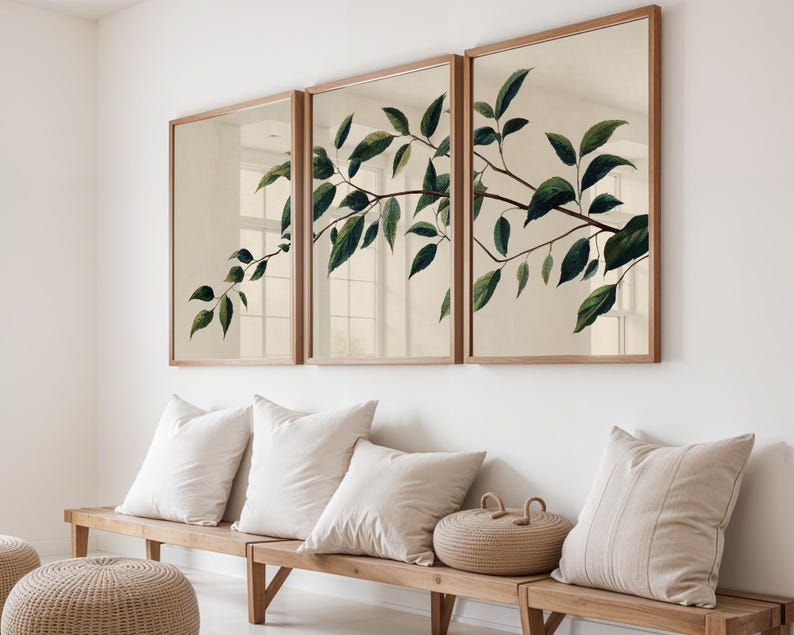 May include: A triptych wall art set featuring a continuous botanical illustration of a leafy branch with dark green leaves on a light beige background, framed in light wood, displayed above a wooden bench with several beige throw pillows.