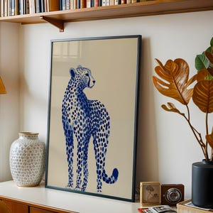 May include: A framed vertical wall art print featuring a blue and white cheetah illustration on a solid beige background. The cheetah is depicted in a standing profile position with its head turned to the right, showcasing a spotted pattern.