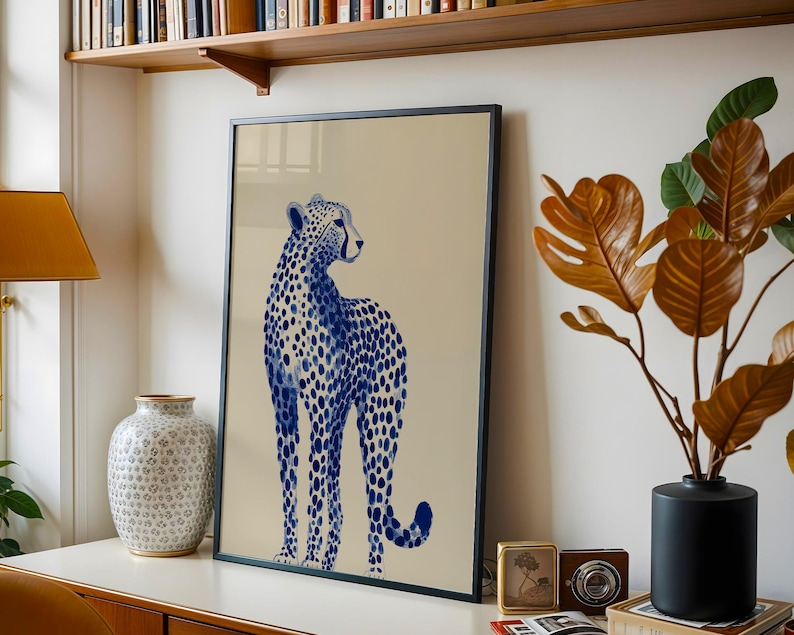 May include: A framed vertical wall art print featuring a blue and white cheetah illustration on a solid beige background. The cheetah is depicted in a standing profile position with its head turned to the right, showcasing a spotted pattern.