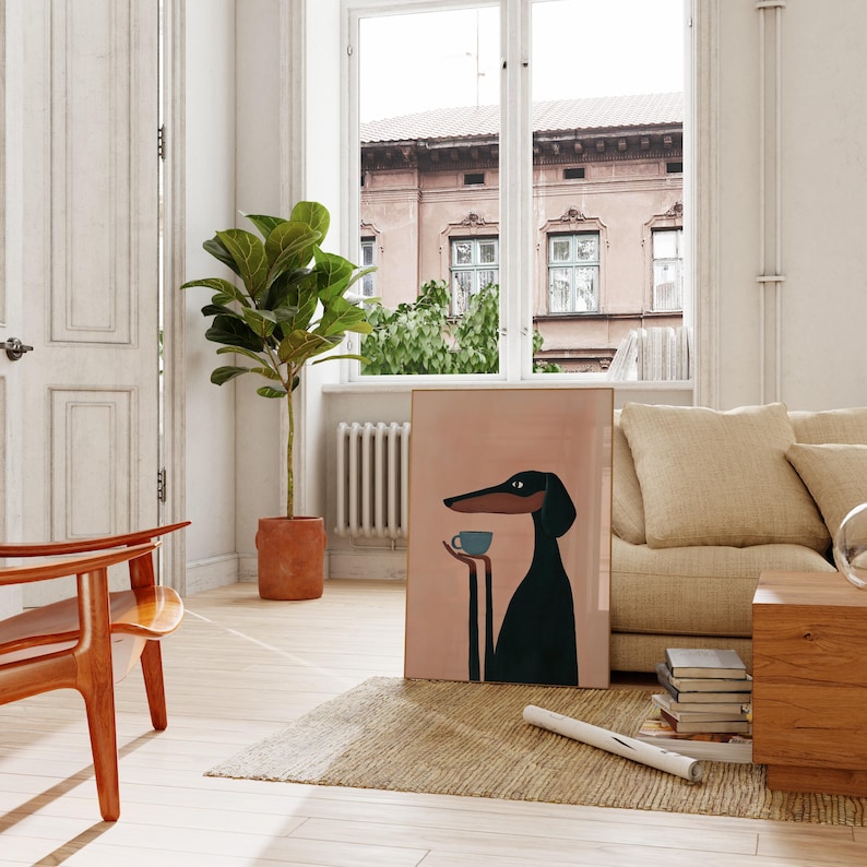 May include: A rectangular framed wall art print featuring a stylized illustration of a black dog with long ears and a long snout, holding a small light blue cup in its paws against a solid light pink background.