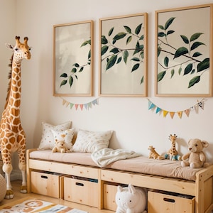 May include: A wooden storage bench with a beige cushion, four wooden storage bins, and three framed botanical prints featuring green leaves on a light background. A large plush giraffe stands beside the bench, with smaller plush toys on top.