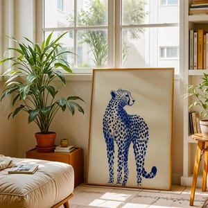 May include: A rectangular framed wall art print featuring a blue and white illustration of a standing cheetah. The cheetah is depicted in shades of blue with a spotted pattern against a solid off-white background, enclosed in a thin gold frame.