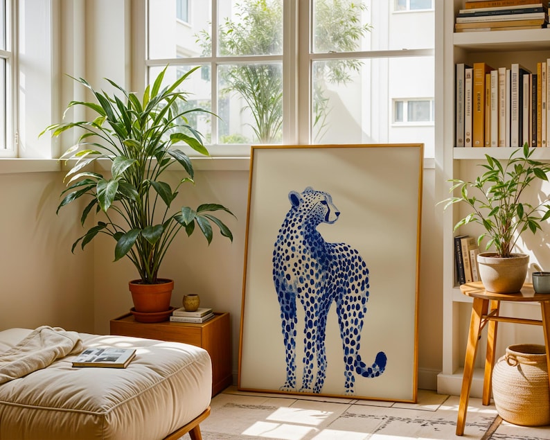 May include: A rectangular framed wall art print featuring a blue and white illustration of a standing cheetah. The cheetah is depicted in shades of blue with a spotted pattern against a solid off-white background, enclosed in a thin gold frame.