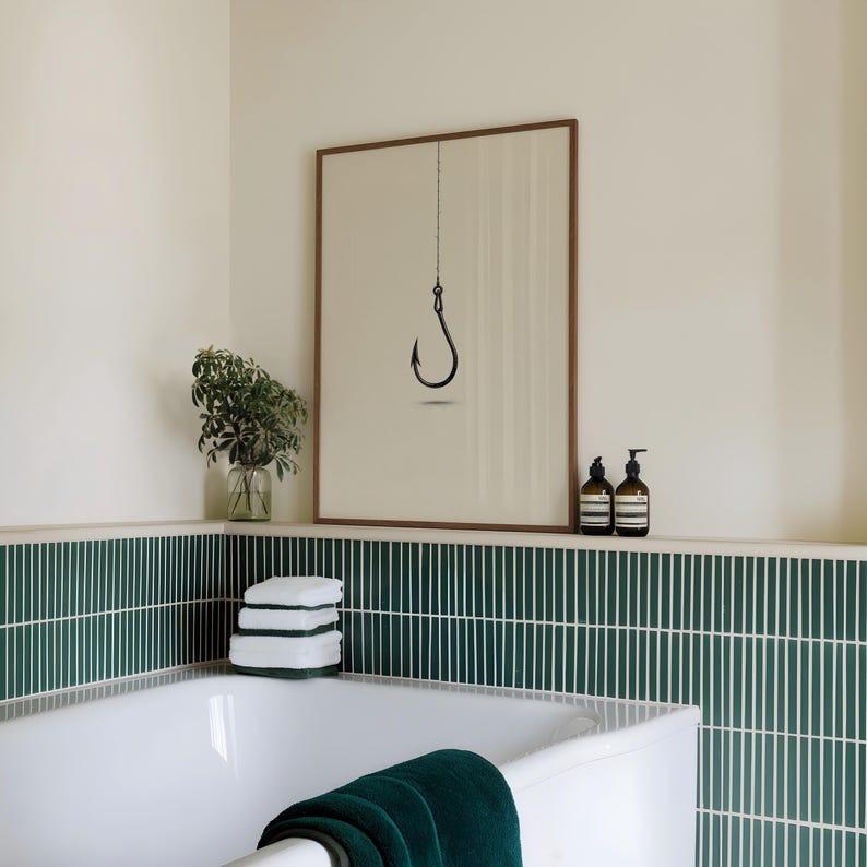 May include: A framed wall art print featuring a minimalist black fishing hook illustration suspended by a thin line against a light beige background, displayed in a bathroom with dark green vertical tile walls and a white bathtub.