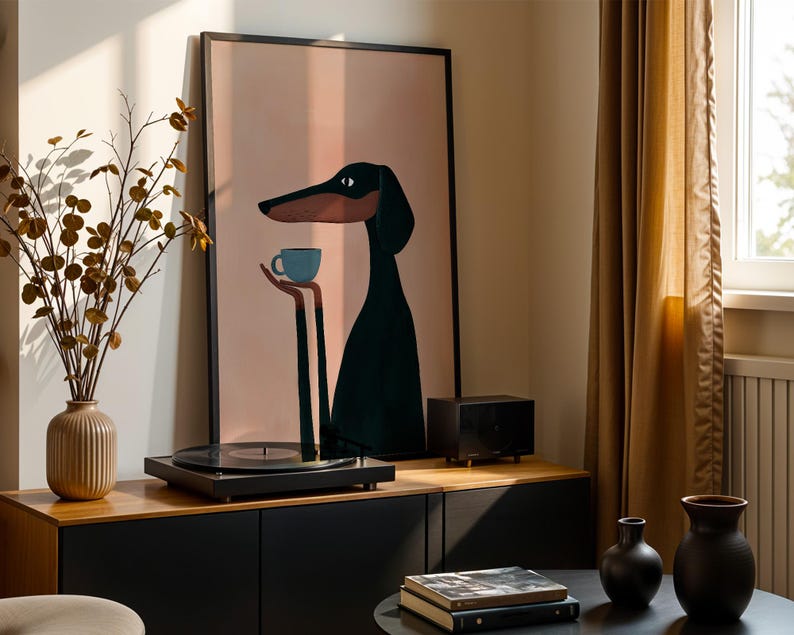 May include: A framed wall art print featuring a stylized illustration of a long-necked black dog with a tan muzzle holding a small light blue coffee cup. The background of the artwork is a solid soft peach color, enclosed in a thin black frame.