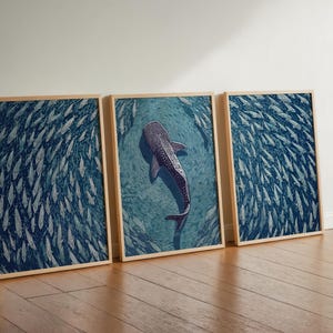 Pode incluir: Um conjunto de tr&ecirc;s quadros de parede emoldurados com uma paleta de cores azul profundo. As duas molduras externas exibem um denso cardume de peixes, enquanto a central retrata um grande tubar&atilde;o-baleia nadando entre peixes menores.