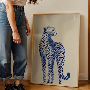 May include: A framed vertical wall art print featuring a blue and white illustration of a cheetah. The cheetah is depicted in a standing profile position with a spotted coat pattern against a light beige background, enclosed in a thin wooden frame.