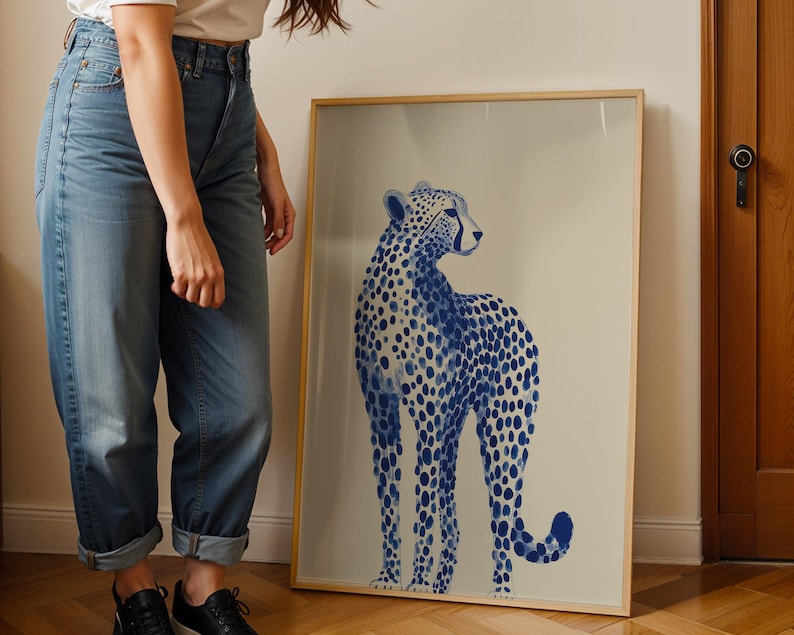 May include: A framed vertical wall art print featuring a blue and white illustration of a cheetah. The cheetah is depicted in a standing profile position with a spotted coat pattern against a light beige background, enclosed in a thin wooden frame.