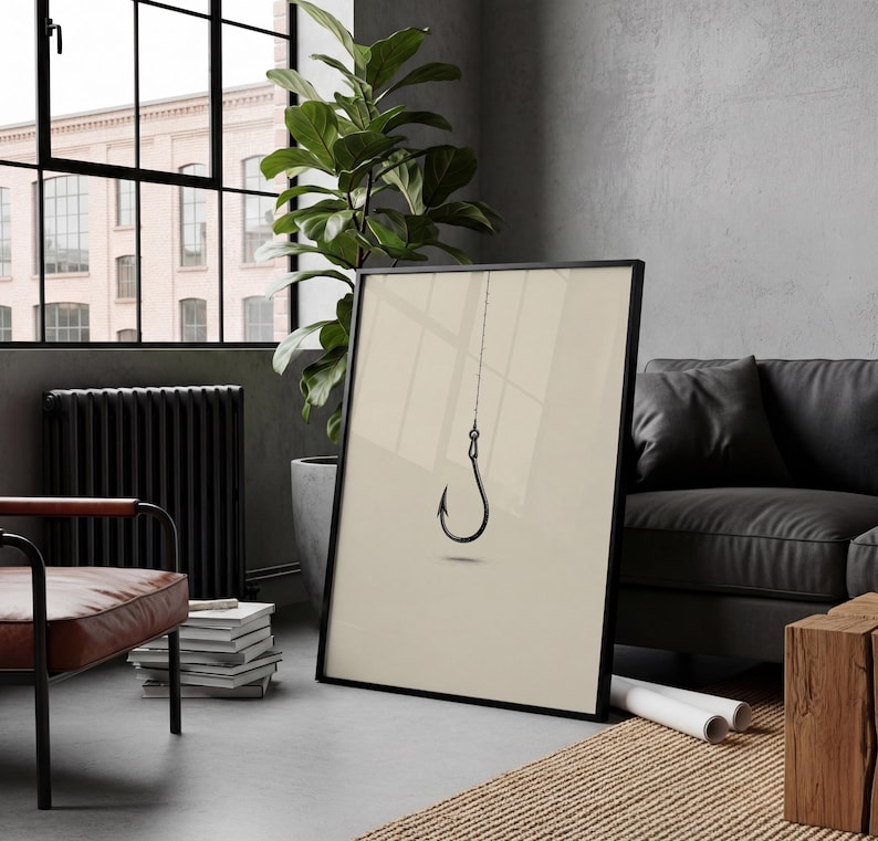 May include: A framed wall art print featuring a minimalist black fishing hook suspended by a thin line against a solid light beige background. The artwork is presented in a thin black frame, showcasing a clean and simple graphic design.