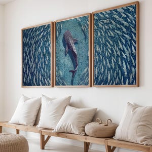 Pode incluir: Um conjunto de arte de parede em tr&iacute;ptico apresentando um grande tubar&atilde;o-baleia nadando em &aacute;guas azul-profundo, cercado por um cardume massivo de peixes menores. As tr&ecirc;s impress&otilde;es retangulares s&atilde;o emolduradas em madeira clara numa parede branca.