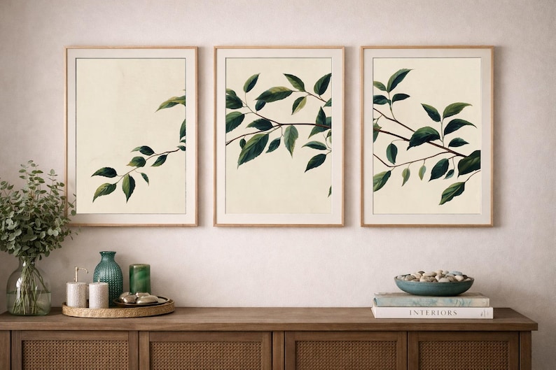 May include: A set of three vertical wall art prints in light wood frames, each featuring a botanical illustration of dark green leaves on a cream background, displayed in a row above a wooden console table with various decorative objects.