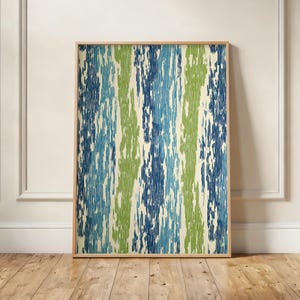 May include: A framed artwork featuring a vertical abstract pattern in shades of blue, green, and cream. The artwork is displayed against a white wall and wooden floor, creating a modern and stylish aesthetic.