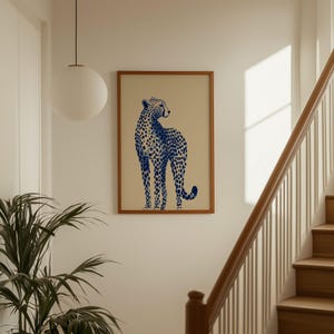 May include: A rectangular wall art print featuring a blue cheetah illustration with dark blue spots on a light beige background, enclosed within a simple wooden frame. The cheetah is depicted in a standing profile position, looking backward.