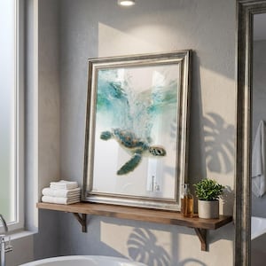 May include: A framed wall art print featuring a sea turtle swimming upward toward the water surface, creating a splash of turquoise and white bubbles. The artwork is encased in a metallic silver frame with a textured, ornate border design.