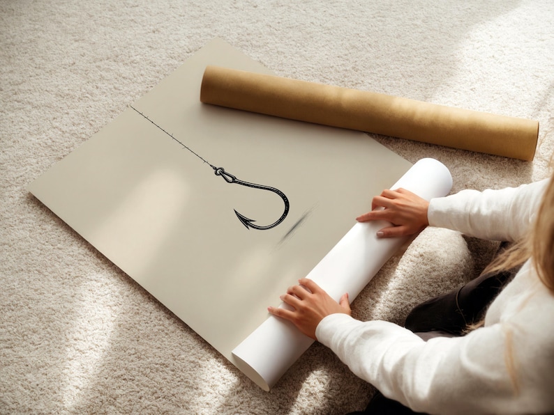 May include: A large, square, beige poster featuring a black line drawing of a single fishing hook attached to a thin fishing line. The poster is displayed flat, with a brown cardboard mailing tube resting nearby on the textured surface.