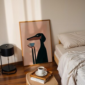 May include: A framed wall art print featuring a stylized illustration of a black and tan dog with long ears holding a small light blue cup. The dog is set against a solid light pink background, and the artwork is enclosed in a thin wooden frame.