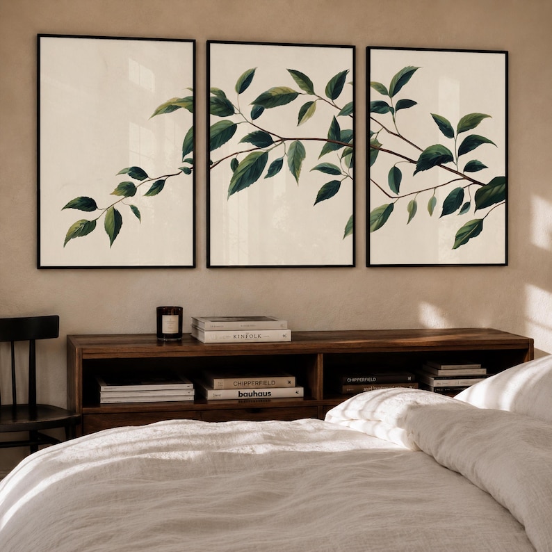 May include: A triptych of three framed wall art prints featuring a continuous botanical illustration of a brown tree branch with dark green leaves against a light cream background, displayed in thin black frames on a neutral wall.
