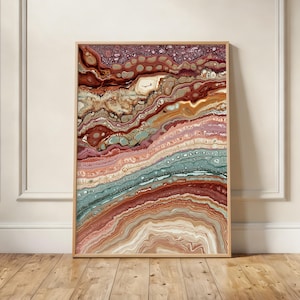 May include: Abstract art print in a wooden frame. The artwork features layered, flowing patterns in shades of red, brown, pink, and teal. The design resembles geological formations or a cross-section of rock strata.