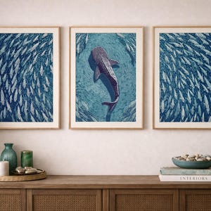 Pode incluir: Um tr&iacute;ptico de tr&ecirc;s impress&otilde;es de arte de parede emolduradas com um tema de oceano azul profundo. As duas impress&otilde;es externas exibem um denso cardume de peixes, enquanto a central retrata um tubar&atilde;o-baleia a nadar entre peixes.
