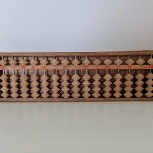 May include: A wooden abacus with a rectangular frame. The abacus has multiple rows of wooden beads in a light brown color. The frame is a darker brown. The abacus is a traditional calculating tool.