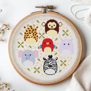 Op de afbeelding: Een borduurring met kruissteek met zes schattige, gepixelde dierenontwerpen: een giraf, aap, vogel, nijlpaard, olifant en zebra. De dieren zijn in verschillende kleuren, omringd door een decoratief patroon.